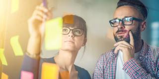 A man and a woman working with post its on a glass wall