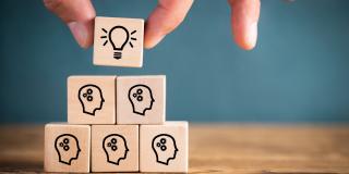 Gestapelte Holzwürfel, die viele denkende Menschen und eine Glühbirne an der Spitze zeigen