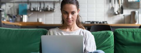 Junge Frau sitzt Laptop im Schneidersitz auf einem Sofa