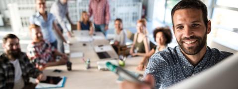 Mehrere Leute an einem Konferenztisch, die in Richtung eines Whiteboards schauen, auf dem ein Mann etwas skizziert.