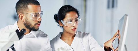 Mann und Frau mit Schutzbrillen stehen vor einem Computerbildschirm in einem Labor