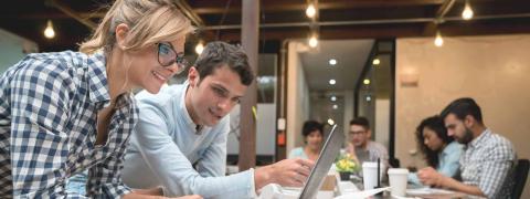 Eine Frau und ein Mann arbeiten in einem Büro an einem Steht mit einem Laptop.
