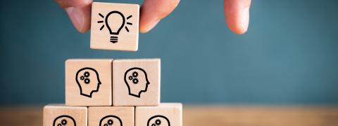 Gestapelte Holzwürfel, die viele denkende Menschen und eine Glühbirne an der Spitze zeigen