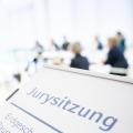 Ein Schild weist auf eine Jurysitzung hin, im Hintergrund sitzt eine Gruppe von Menschen an Tischen